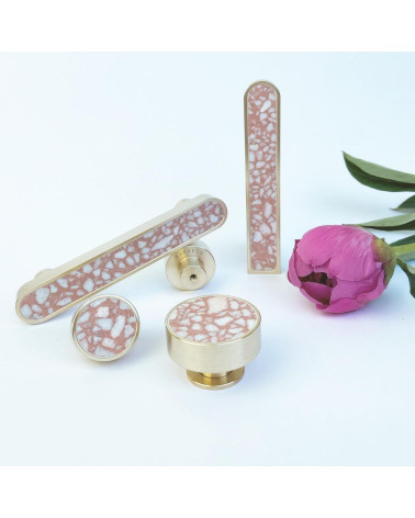 Bouton de meuble en laiton et Pink Terrazzo poignée design disposé à côté d'une fleur sur fond blanc